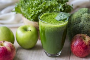 glass of green juice with apples and vegetables around it