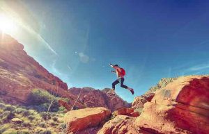 man jumping red rocks sunshine happy energetic