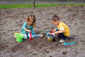 boy and girl playing in sandbox with pails and shovels