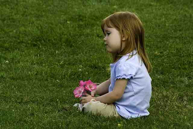 little girl holding flowers sitting on a lawn