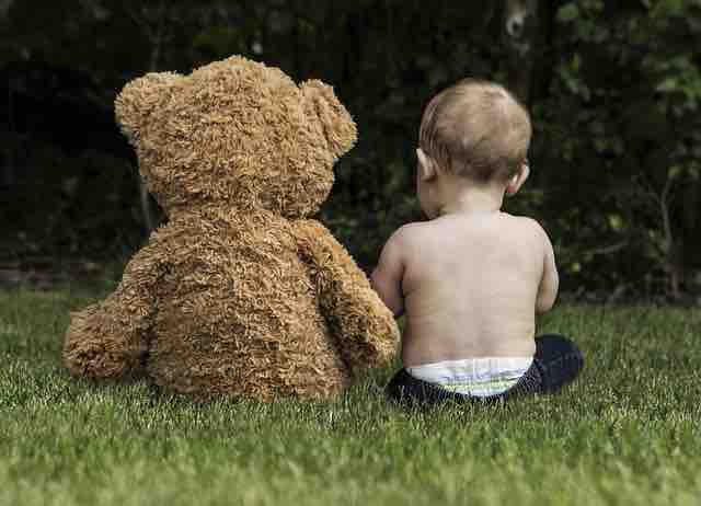 toddler sitting on a lawn with a large teddy bear