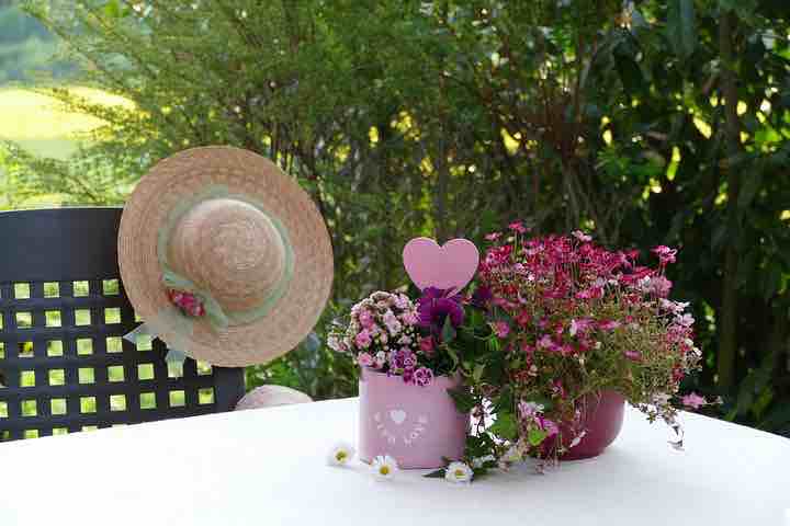 Two vases of flowers, a sunhat hanging over a chair with a table in a garden